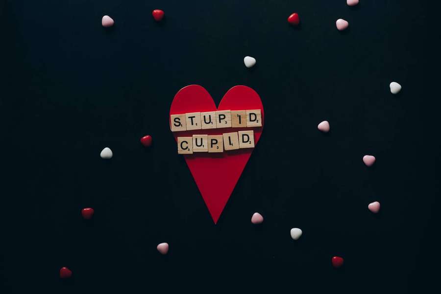 Red paper heart with 'STUPID CUPID' tiles surrounded by small hearts on dark background. — Stupid Background