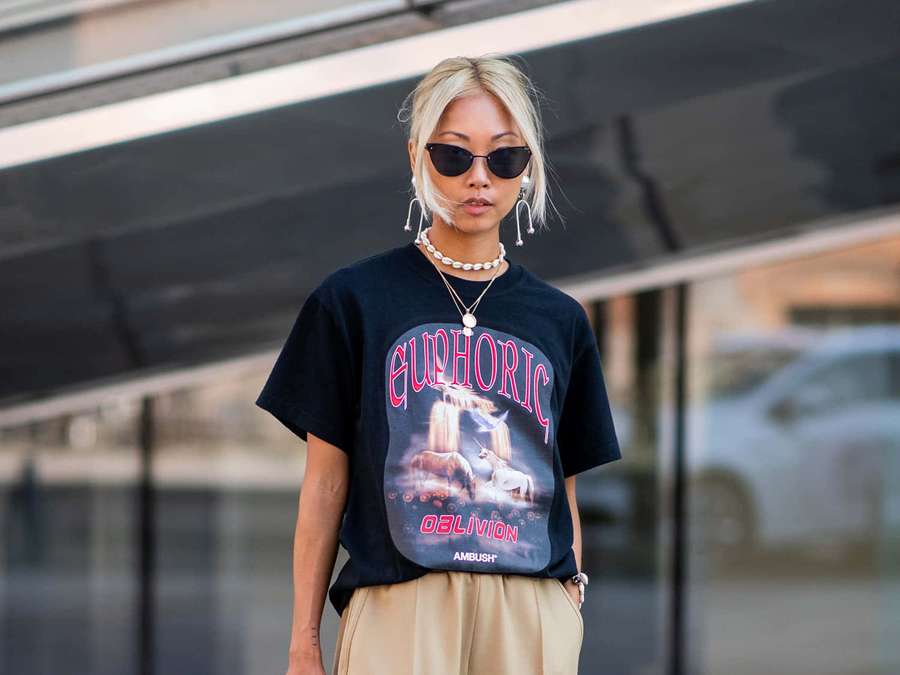 Person wearing sunglasses and a black t-shirt with a unicorn graphic standing in front of a glass building. — Style Background