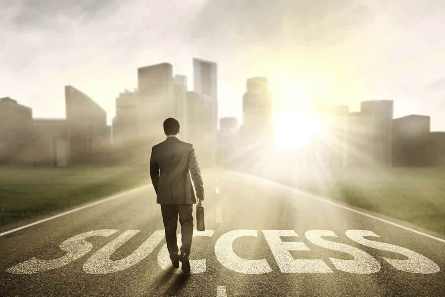 Man in suit walking on road with 'SUCCESS' painted toward city at sunrise. — Successful Wallpaper