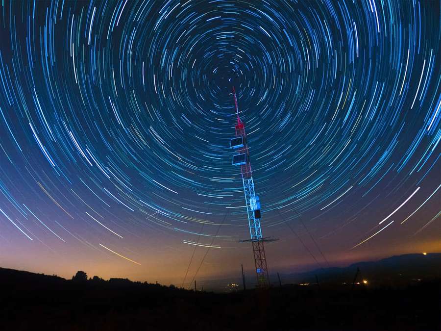 Radiotårn under hvirvlende stjernespor ved skumring — Succinct Wallpapers