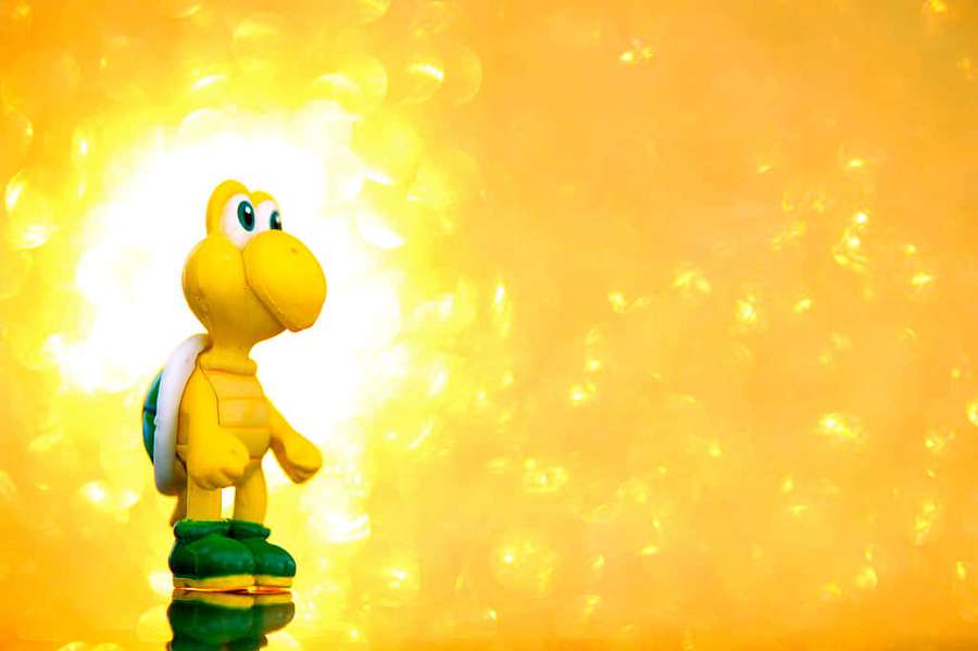 Gelbe Koopa Troopa-Spielfigur mit grünem Panzer und Stiefeln auf reflektierender Oberfläche vor goldenem Licht. — Super Mario Odyssee Wallpaper