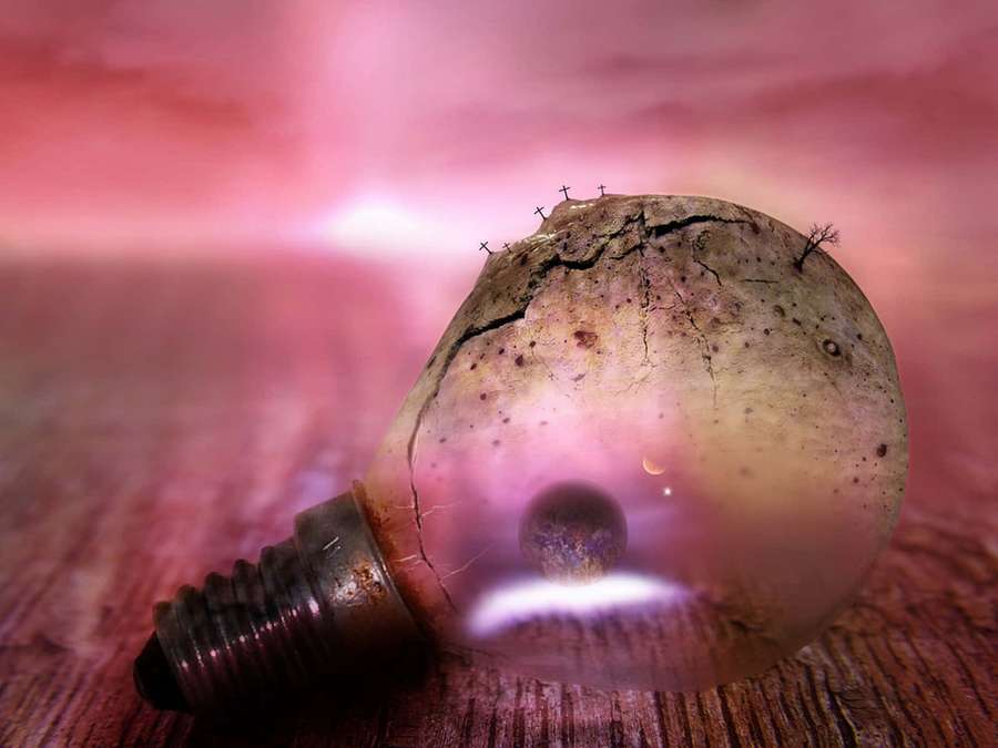 Cracked light bulb containing a miniature alien planet and moon on wooden surface. — Surrealism Wallpaper
