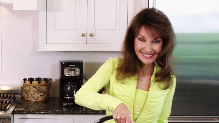 Frau in limettengrünem Oberteil lächelt in moderner Küche mit Kaffeemaschine. — Susan Lucci Bilder