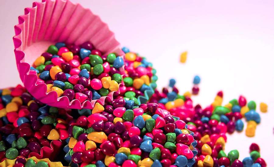 A pink cupcake liner overflowing with colorful candy-coated chocolates. — Sweet Background