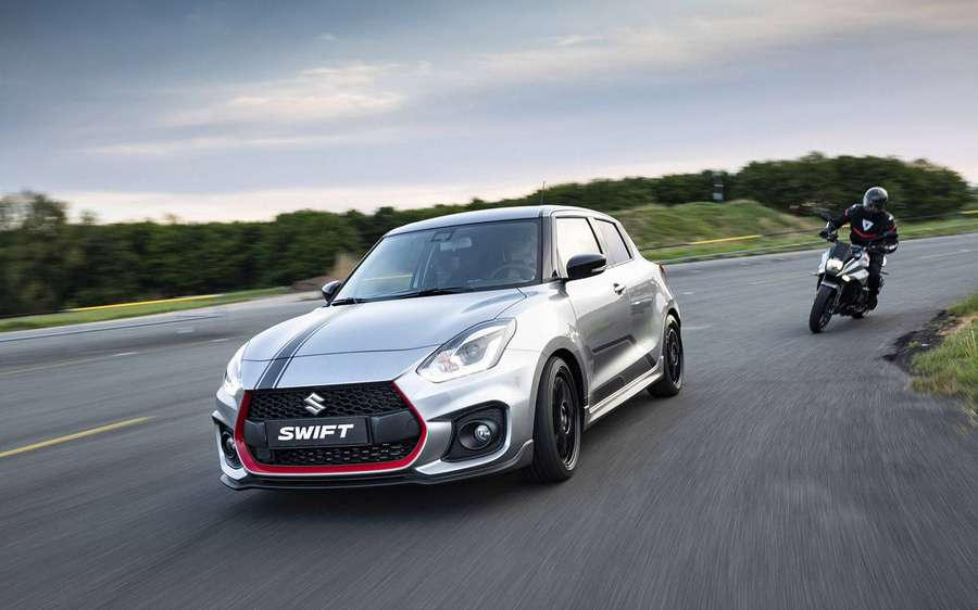 Silver Suzuki Swift car speeding on road with motorcycle rider beside it. — Swift Picture