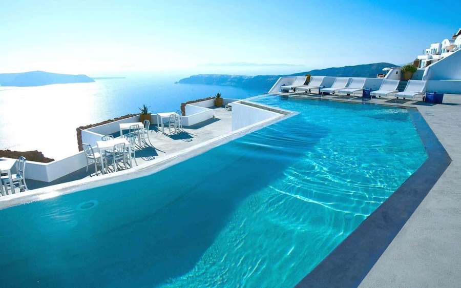 Infinity pool overlooking the Aegean Sea with white lounge chairs and tables. — Swimming Background