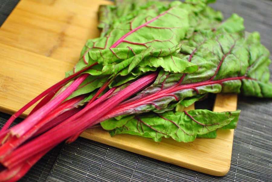 Acelga fresca con tallos rojos y hojas verdes sobre una tabla de cortar de madera. — Swiss Chard Fondos de pantalla