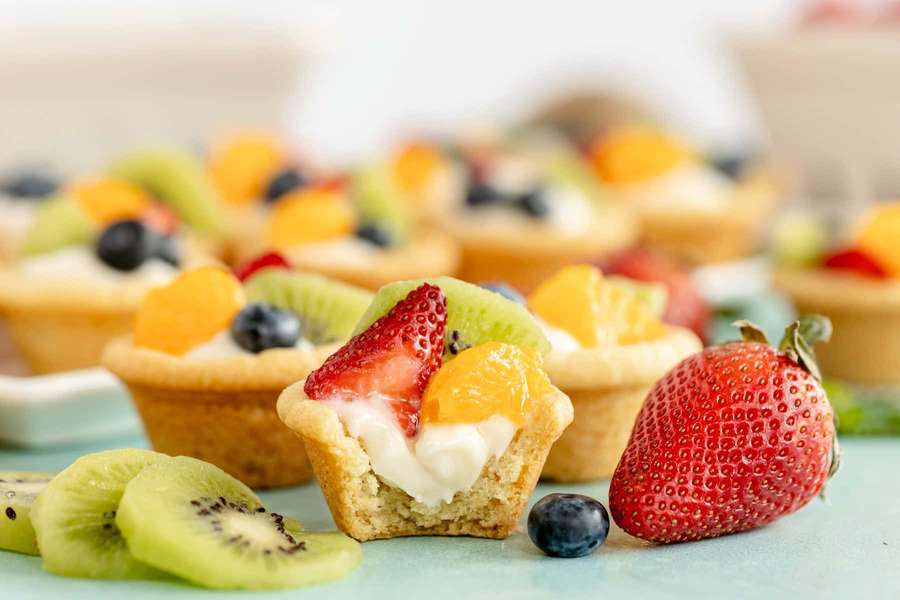 Colorful fruit tarts with fresh berries and sliced kiwi on a light blue surface. — Tart Wallpaper