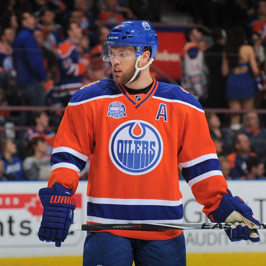 Jääkiekkoilija Oilers-paidassa pitää mailaa jäällä ottelun aikana. — Taylor Hall Taustakuvat