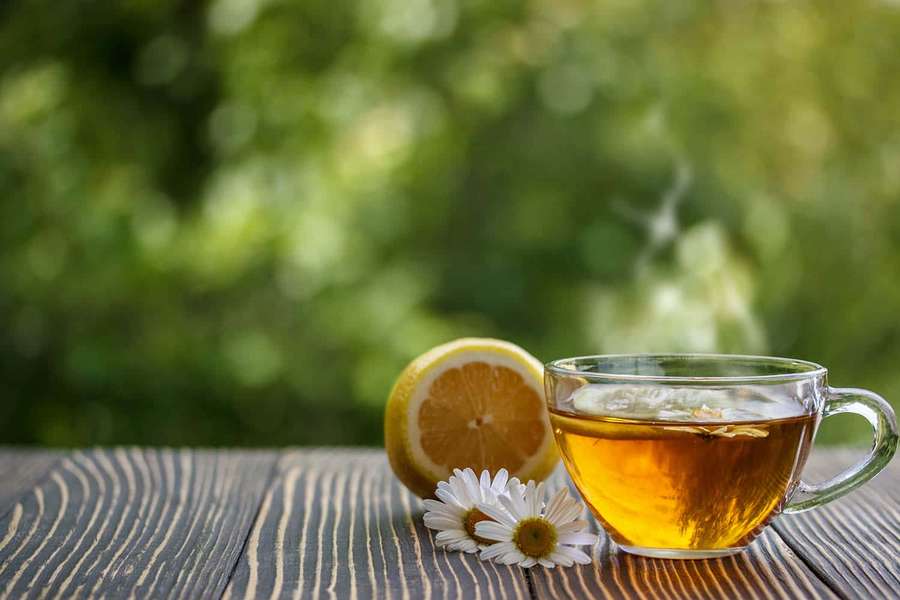 A cup of tea with lemon and chamomile flowers on a wooden table outdoors. — Tea Background