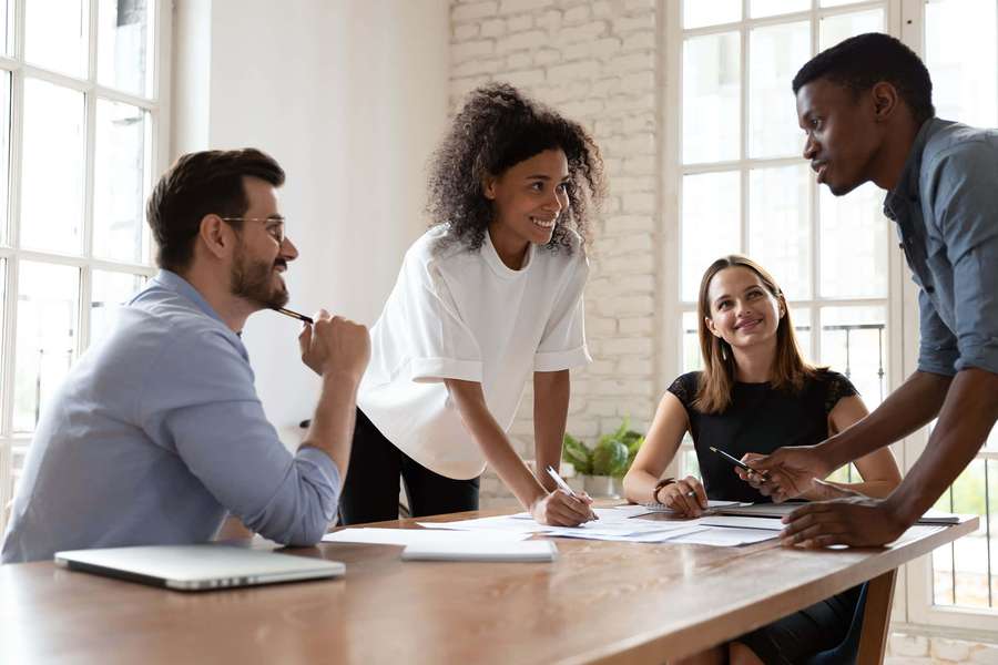 Four colleagues in a modern office discussing documents at a wooden table. — Team Picture