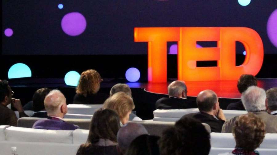 Audience watching a TED talk on a stage with glowing logo and colorful orbs. — Ted Talk Background
