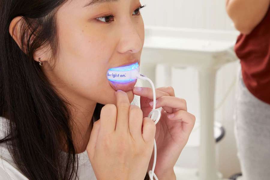 Woman using a blue light oral appliance with assistance in a dental clinic. — Teeth Whitening Wallpaper