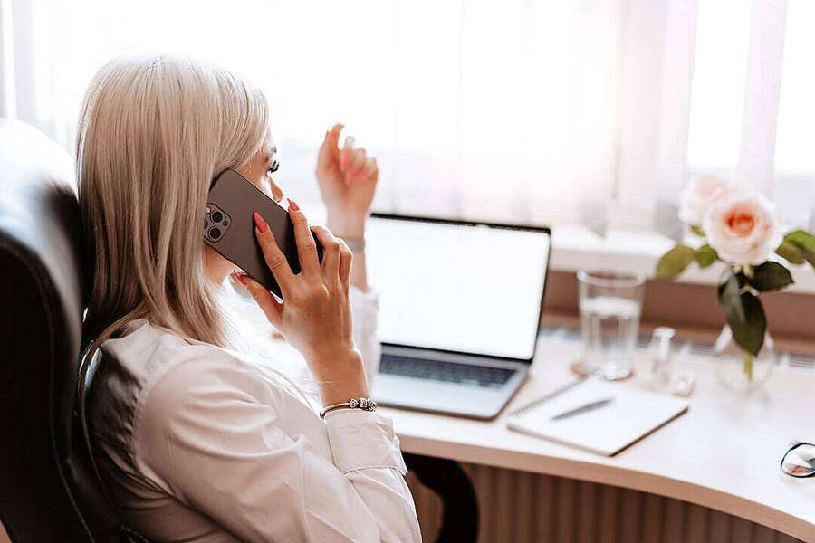 Blonde Frau am Telefon am Schreibtisch mit Laptop und rosa Rose im Sonnenlicht — Telefonanruf Wallpaper
