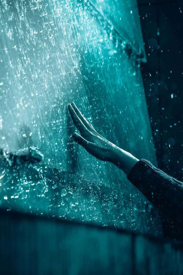 Una mano tocando suavemente el agua turquesa que fluye en un entorno oscuro y reflectante. — Teléfono azul Fondos de pantalla