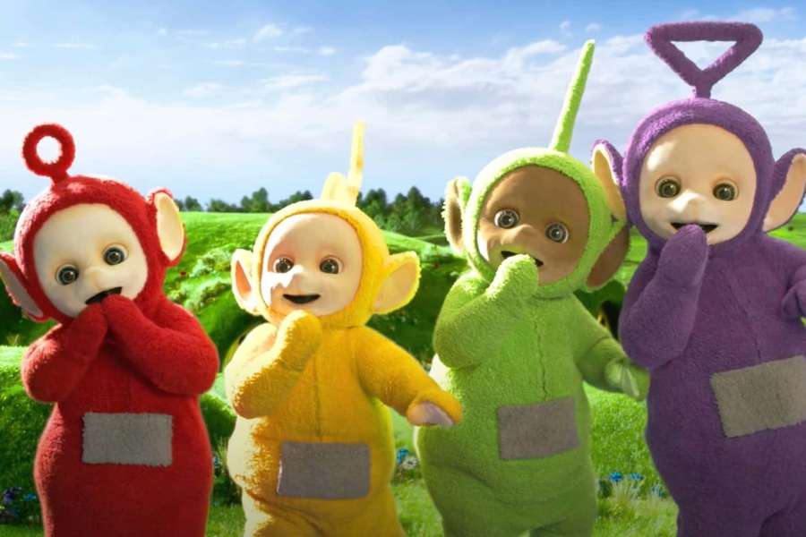 Four colorful Teletubbies standing in a grassy field on a sunny day. — Teletubbies Background
