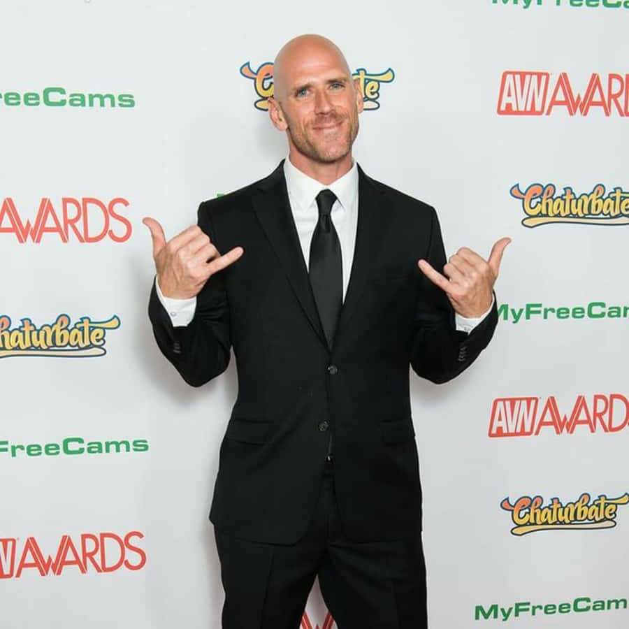 Mann in schwarzem Anzug posiert bei den AVN Awards mit Handgesten. — Teppich Wallpaper