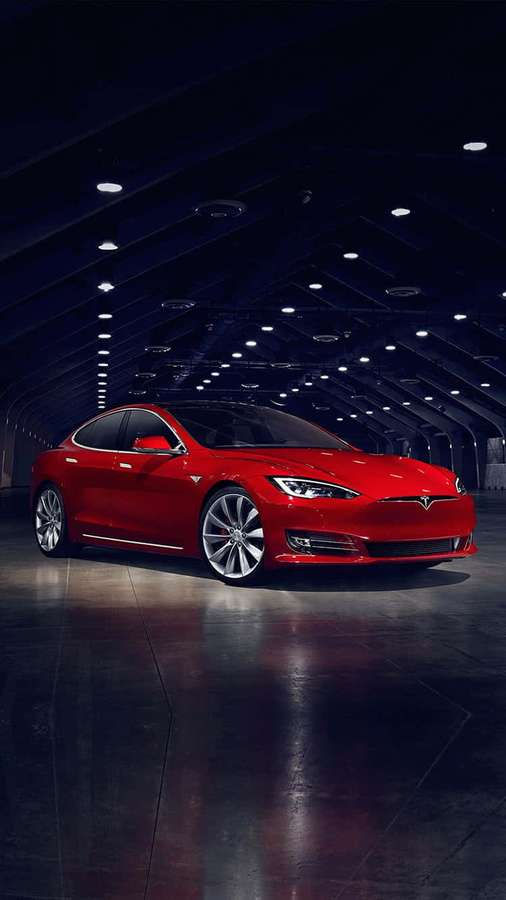 Red Tesla Model S in a dark industrial garage with reflective floor. — Tesla iPhone Wallpaper
