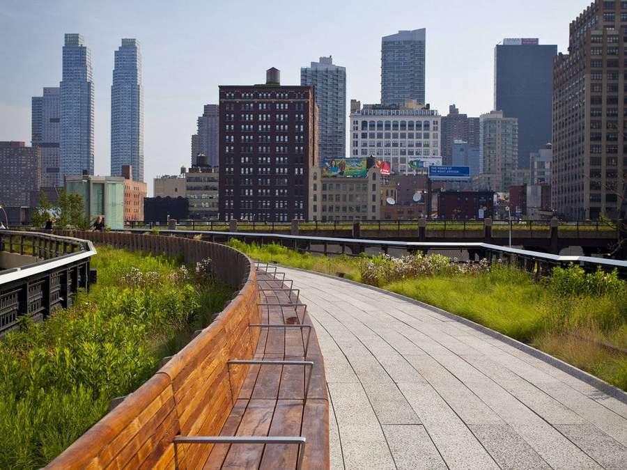 Curved wooden bench along a grassy path with city buildings in background. — The High Line Wallpaper