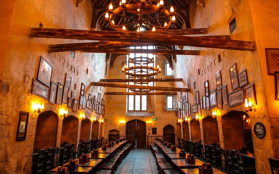 Medieval dining hall with stone walls wooden beams and candlelit tables. — The Leaky Cauldron Wallpaper