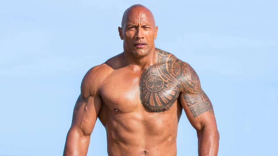 Ein muskulöser Mann mit Stammestätowierungen steht draußen unter blauem Himmel. — The Rock Bilder
