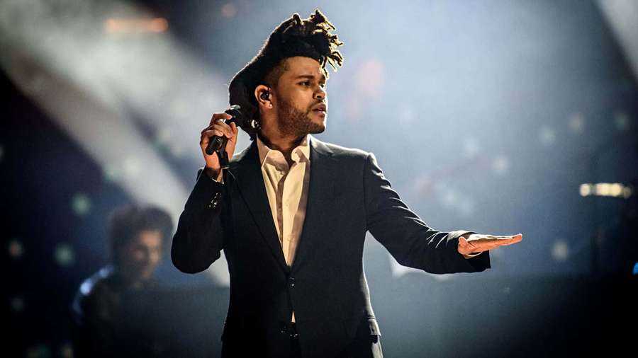 Singer The Weeknd performs on stage in a black suit under bright lights. — The Weeknd Background