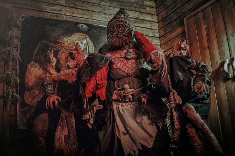 Three horror figures in bloodied costumes with a wicker mask stand in a dark wooden room. — The Witcher Crones Wallpaper
