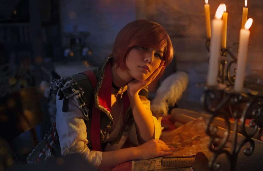 Person with red hair in cosplay leans on table beside lit candles in dim room. — The Witcher Shani Wallpaper