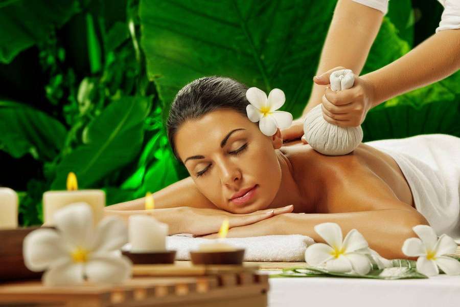 Woman enjoying a herbal massage with frangipani flowers and candles in a spa. — Therapy Wallpaper