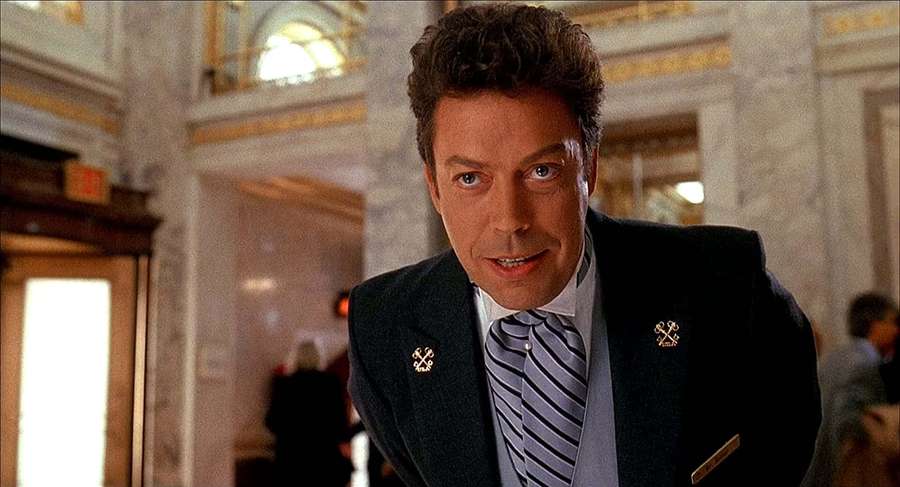 Man in suit and striped tie with gold pins in marble hallway — Tim Curry Wallpaper