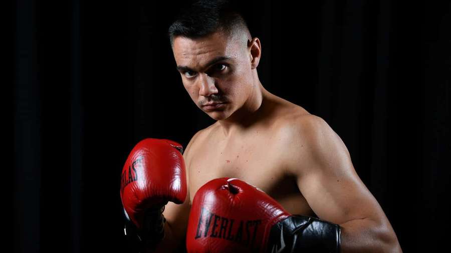 A focused male boxer in red gloves poses against a black background. — Tim Tszyu Wallpaper