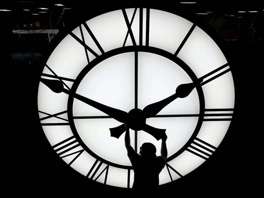 Arbeitersilhouette vor einem riesigen beleuchteten Zifferblatt in einer Fabrik. — Time Clock Bilder Hintergrund Wallpaper