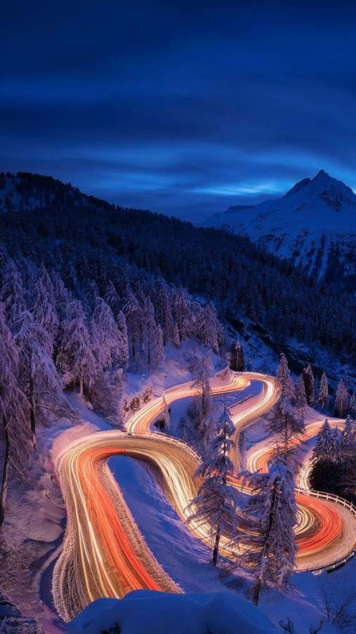 Winding snowy mountain road at twilight with glowing car light trails. — Time lapse Wallpaper