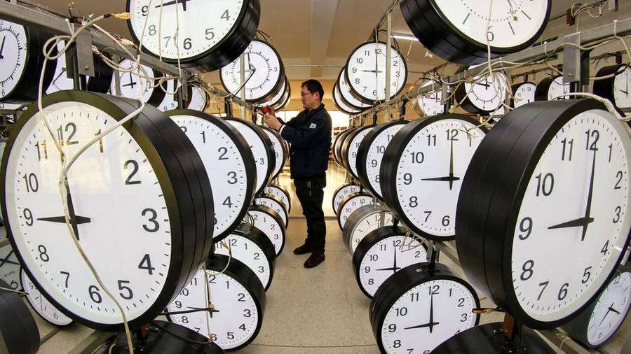 Technician adjusting clocks in a factory filled with hanging analog timepieces. — Time Wallpaper