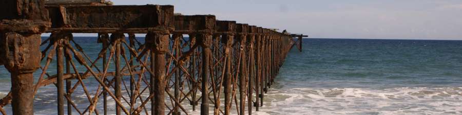 Rusty pier stretching into ocean with crashing waves and clear sky — Togo Wallpaper