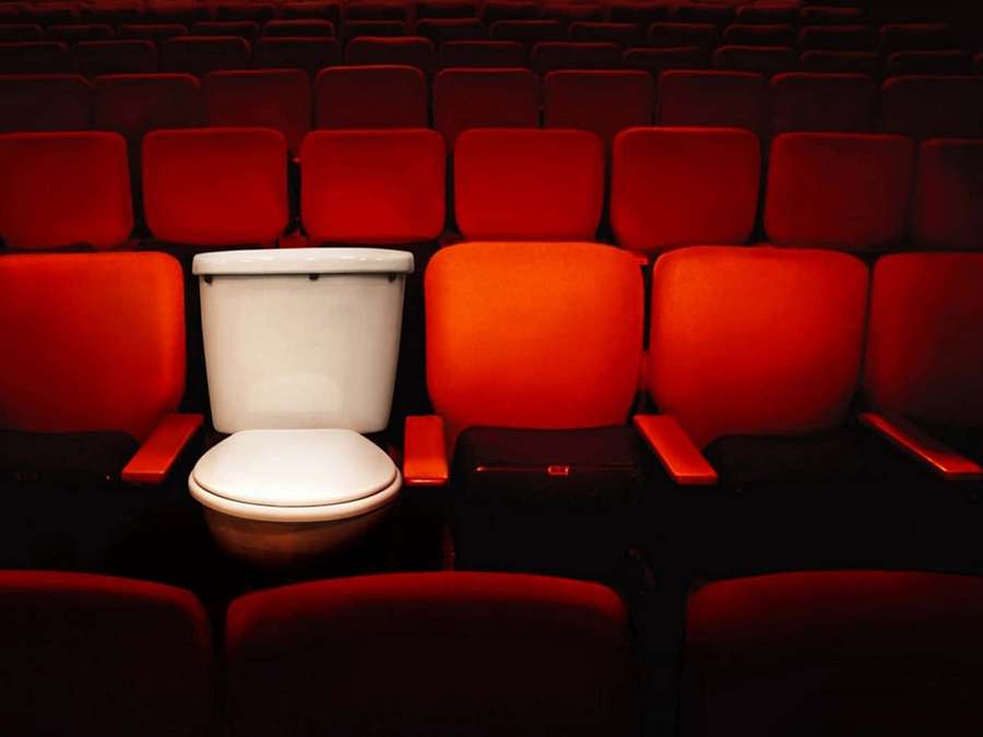 A white toilet placed among red theater seats in a dark auditorium. — Toilet Background