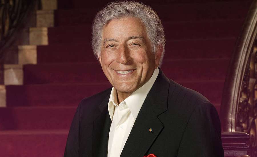 A smiling man in a suit stands in front of a red carpeted staircase. — Tony Bennett Wallpaper