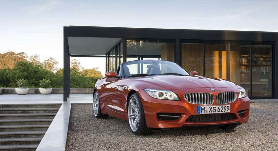 Punainen BMW Z4 avoauto pysäköitynä modernin lasitalon edessä auringonlaskun aikaan. — Top 10 Auto Taustakuvat
