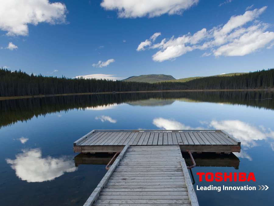 Wooden dock leading into a serene lake reflecting blue sky and clouds. — Toshiba Wallpaper