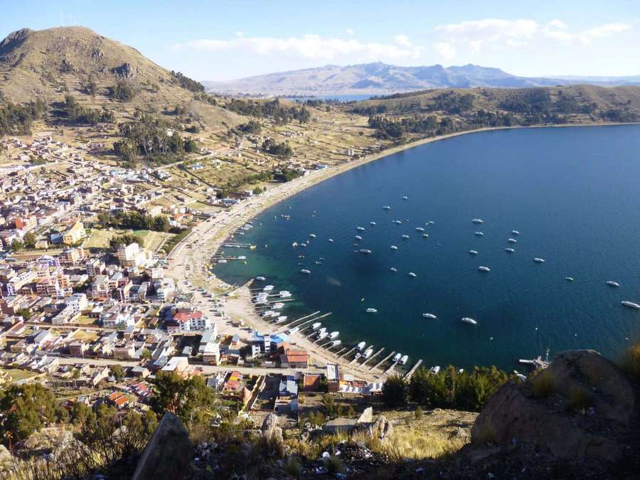 A scenic lakeside town with boats and surrounding mountains under a clear sky. — Towns Background