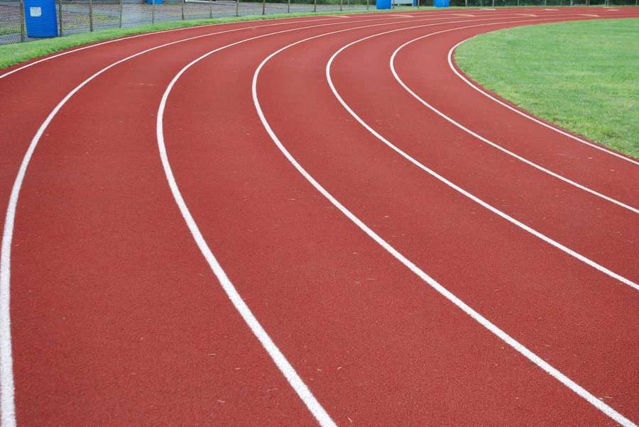 Red athletic track with white lanes curving beside green grass field. — Track Background