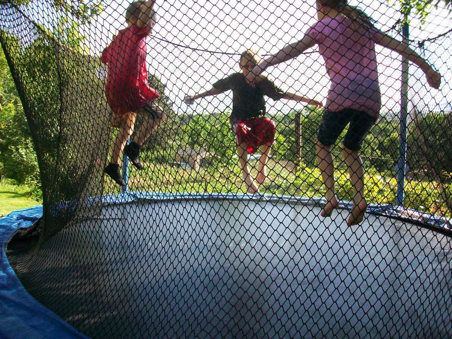 Tres niños rebotando en una cama elástica en un patio trasero soleado. — Trampolín Fondos de pantalla