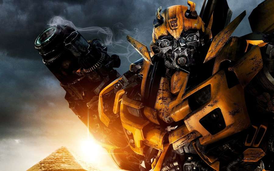 A yellow and black robot with smoke rising from its arm against a stormy sky with a glowing pyramid. — Transformers Background