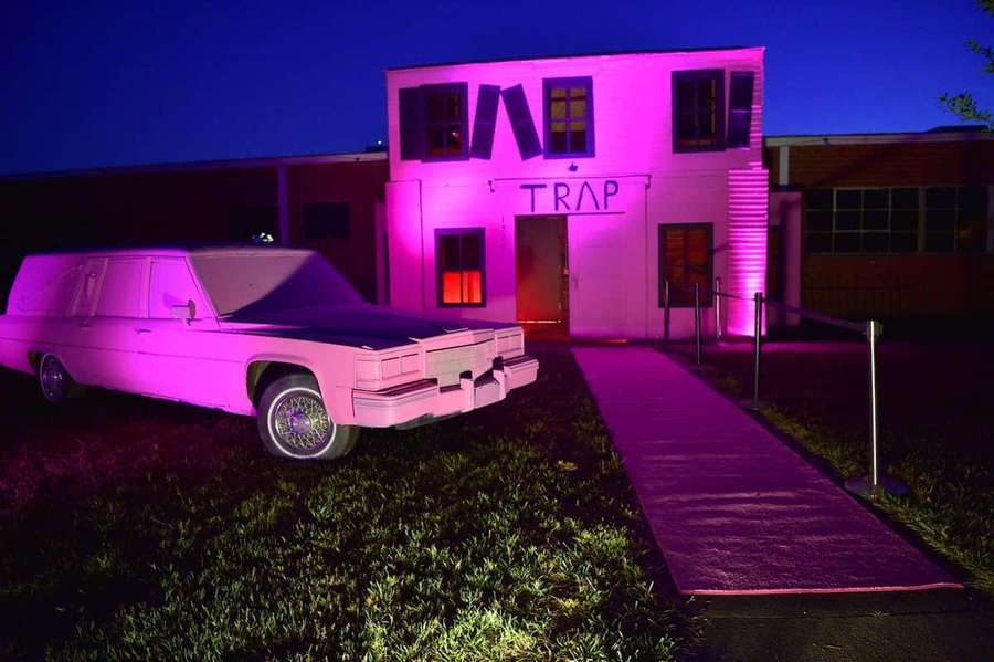 Pink-lit hearse parked before a building labeled trap at night. — Trap House Wallpaper