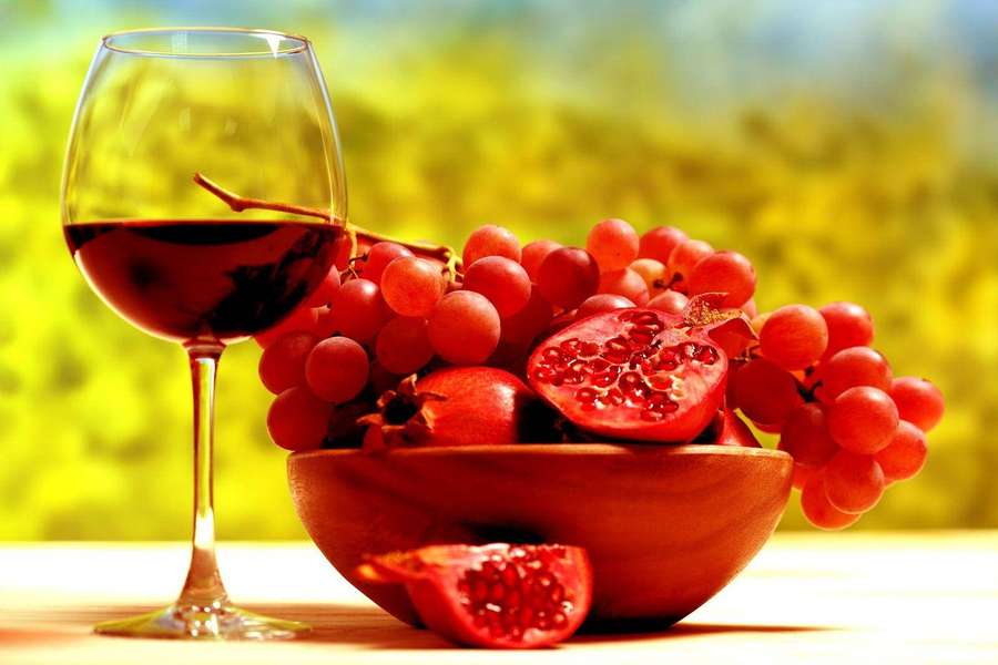 Ein Glas Rotwein neben einer Schale mit Trauben und Granatäpfeln auf einem Holztisch. — Trauben Wallpaper