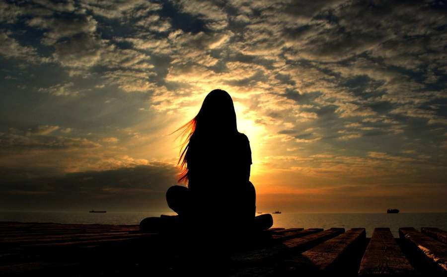 Person sitzt auf Steg und beobachtet Sonnenuntergang über dem Meer mit Wolken — Trauriges Mädchen Bilder Wallpaper