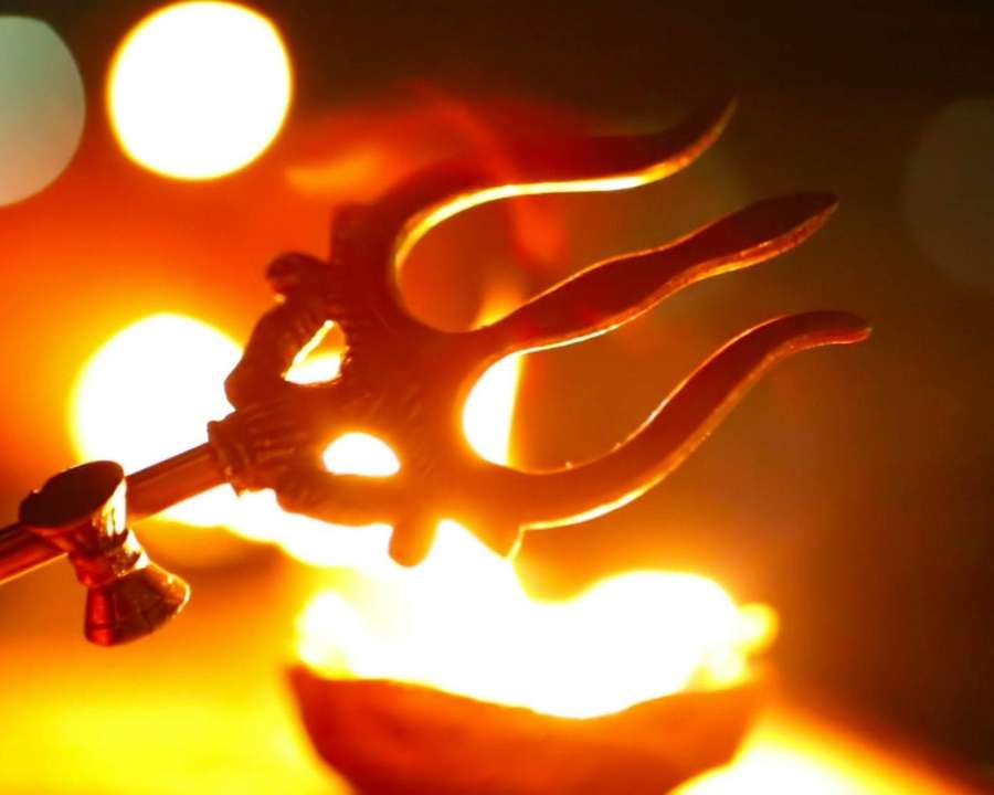 A trident silhouette glowing against warm lights and fire. — Trishul Wallpaper