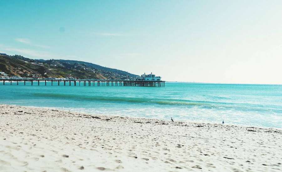 A sunny beach with turquoise water and a long pier extending into the ocean. — Tropical Beach Wallpaper