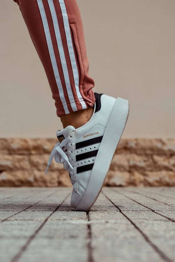 Nahaufnahme eines weißen adidas Superstar Sneakers auf Steinpflaster mit rostfarbenen Trainingshosen. — Turnschuh Wallpaper
