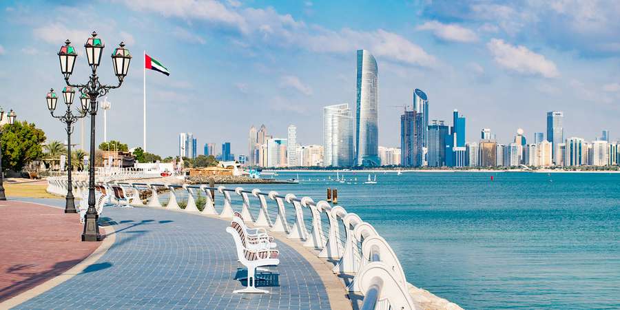 Calçada marítima curva com bancos e lampadários com vista para um horizonte moderno da cidade e água turquesa. — Uae Papéis de Parede